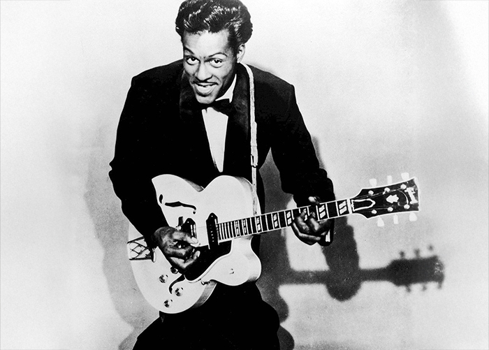 An overhead black and white shot of Chuck Berry sitting down holding an acoustic guitar.